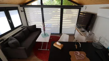Gemütlicher Wohnbereich mit Sofa, Fernseher und Holzdachschräge, hell durch große Fenster.