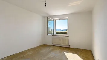 Helles, leeres Schlafzimmer mit Rohboden, weißen Wänden und einem Fenster mit Blick ins Grüne.