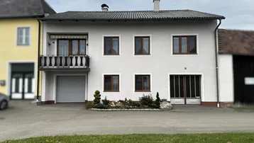 Weißes Mehrfamilienhaus mit braunen Fenstern, Balkon und integrierter Garage.