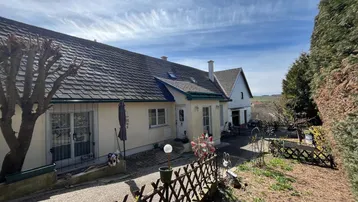 Charmantes Einfamilienhaus mit Satteldach und gepflegtem Vorgarten unter blauem Himmel.