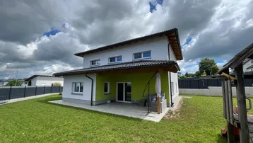 Modernes Einfamilienhaus mit weißer Fassade, grüner Akzentwand und großem Gartenbereich mit Terrasse.