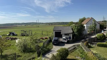 Weitblick über das Anwesen mit Garage, Zufahrt und angrenzenden Feldern unter blauem Himmel.