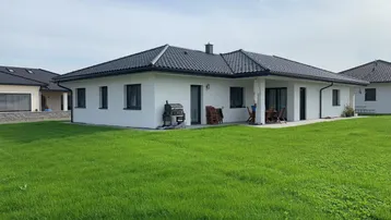 Modernes Einfamilienhaus mit gepflegtem Rasen und einer Terrasse mit Gartenmöbeln.