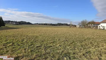 Weitläufiges Grundstück mit Blick auf die umliegende Landschaft und entfernte Häuser unter blauem Himmel.