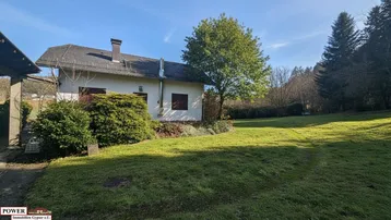Großzügiger Gartenbereich mit Rasenfläche und Baumbestand neben dem Haus unter blauem Himmel.