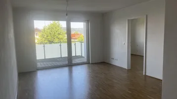 Helles Zimmer mit Holzboden und Zugang zu einem Balkon, bietet einen grünen Ausblick.
