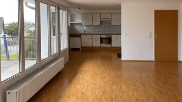 Heller offener Wohn-Essbereich mit Parkettboden und Zugang zum Balkon, inklusive integrierter Küche.