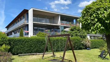 Modernes Mehrfamilienhaus mit großen Balkonen und einem gepflegten Gartenbereich inklusive Schaukel für Kinder.