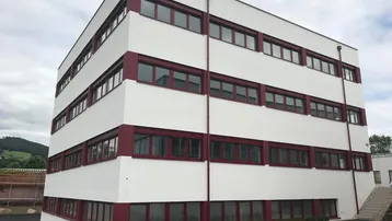 Modernes Bürogebäude mit weißer Fassade und roten Fensterrahmen unter bewölktem Himmel.