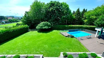 Weitläufiger Garten mit großem Rasen, Poolbereich und altem Baumbestand unter blauem Himmel.