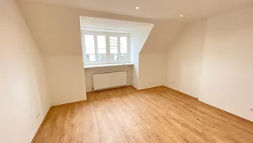 Helles Zimmer mit Dachschräge, Holzfußboden und Fenster, ideal als Schlaf- oder Arbeitszimmer.