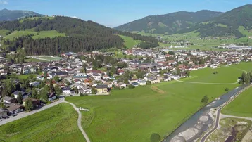 Luftaufnahme einer malerischen Stadt in einem Tal, umgeben von grünen Hügeln und Bergen mit einem Fluss.
