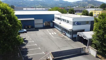 Luftaufnahme eines Gewerbegebäudes mit Parkplätzen und umliegender grüner Landschaft.