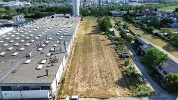 Luftaufnahme eines großen Industriegeländes mit angrenzendem unbebautem Grundstück und Wohnbebauung im Hintergrund.