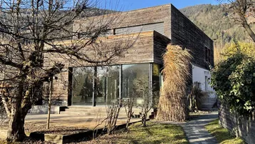 Modernes Haus mit Holzfassade und großen Glasfronten, umgeben von einem gepflegten Garten.