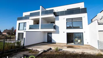 Moderne weiße Wohnanlage mit Balkonen und einer unfertigen Terrasse im Erdgeschoss.