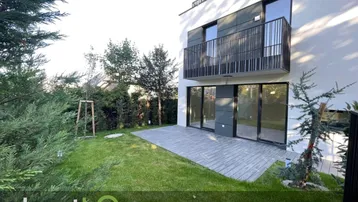 Moderne Hausfassade mit gepflegtem Rasen, Terrasse und Balkon in ruhiger Umgebung.