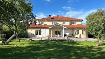 Großzügiges Einfamilienhaus mit weitläufigem Garten und gepflegter Rasenfläche unter blauem Himmel.