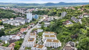 Luftaufnahme einer modernen Wohnanlage eingebettet in eine grüne Hügellandschaft mit Stadtblick.
