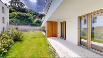 Moderne Wohnanlage mit privatem Gartenbereich und gepflasterter Terrasse, umgeben von grüner Landschaft.