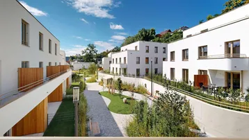 Luftaufnahme einer modernen Wohnsiedlung in einer grünen Hügellandschaft mit Stadtblick.