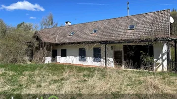 Ländliches Anwesen mit altem Haus und verwildertem Garten unter blauem Himmel.