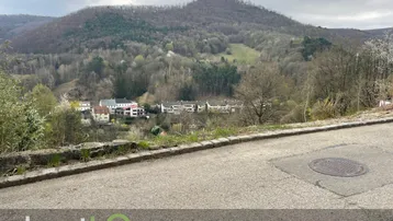 Panoramablick über ein bewaldetes Tal mit Häusern und Bergen unter einem bewölkten Himmel.