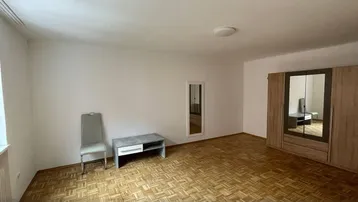 Geräumiges Zimmer mit hellem Parkettboden, weißen Wänden und einem großen Spiegelschrank.