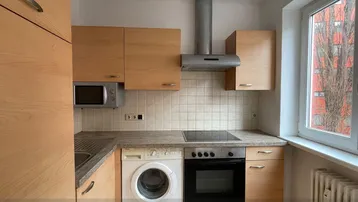 Funktionale Küche mit Holzschränken, Einbaugeräten und einem Fenster mit Blick nach draußen.