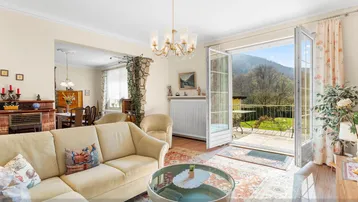Helles Wohnzimmer mit Sofa, Teppich und Zugang zu einem Balkon mit Bergblick.