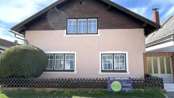 Vorderansicht eines Einfamilienhauses mit rosafarbener Fassade, Holzdachgiebel und kleinem Vorgarten.