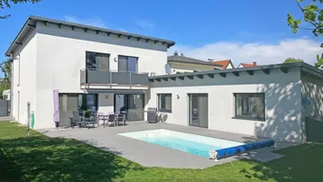 Moderne Villa mit Pool, Terrasse und Balkon, umgeben von einem gepflegten Garten.