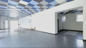 Geräumiger, leerer Gewerberaum mit auffälliger Deckenverkleidung und großen Fenstern.