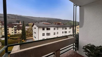 Blick vom Balkon auf die umliegenden Wohngebäude und grüne Hügellandschaft.