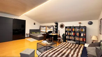 Geräumiges Schlafzimmer mit Dachschräge, Holzboden und integriertem Wohnbereich.