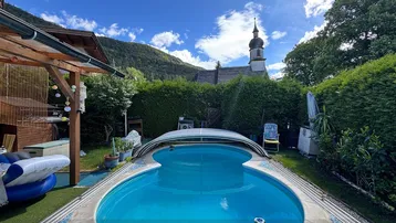 Großer Gartenbereich mit Pool und Blick auf die umliegende Berglandschaft und eine Kirche.