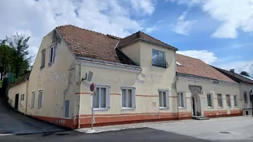 Altes Gebäude mit verputzter Fassade und Ziegeldach, das Renovierungsbedarf aufweist.