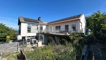 Hausfassade mit Balkon, Solaranlagen auf dem Dach und Blick ins Grüne.