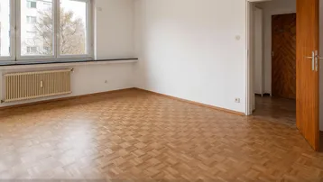 Heller, leerer Raum mit Parkettboden und großen Fenstern, ideal als Wohnzimmer.