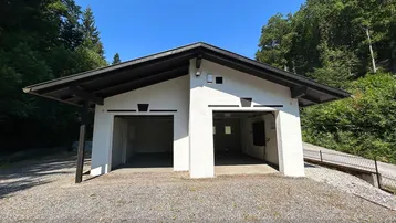 Offene Doppelgarage mit zwei Einfahrten, umgeben von grünen Bäumen unter strahlend blauem Himmel.