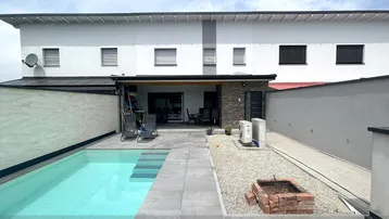 Moderner Außenbereich mit Swimmingpool, gefliester Terrasse und Feuerstelle hinter dem Haus.