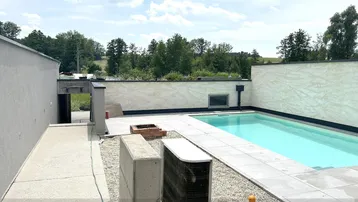 Hinterhof mit Swimmingpool, gefliester Fläche und Blick auf die umliegende grüne Landschaft.