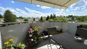 Möblierter Balkon mit Markise, Pflanzen und weitem Blick über die Wohnsiedlung und grüne Umgebung.