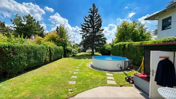 Gepflegter Gartenbereich mit Rasenfläche, Hecken, einem Aufstellpool und Gartenhaus unter blauem Himmel.