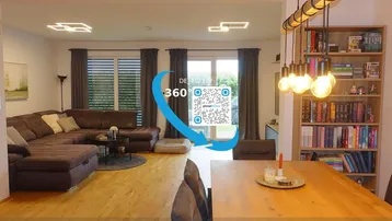 Heller, offener Wohn- und Essbereich mit Holzboden, großem Sofa, Esstisch und modernen Leuchten.