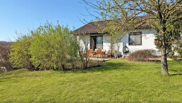 Sonnige Terrasse mit Gartenmöbeln und weitläufigem Rasenbereich vor einem gepflegten Einfamilienhaus.