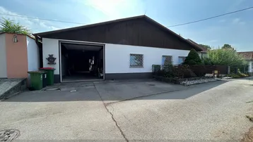 Geräumige Garage mit offenem Tor und gepflasterter Zufahrt, umgeben von kleinen Grünflächen.