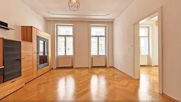 Helles Wohnzimmer mit Fischgrätparkett, Stuckdecke und hohen Fenstern.