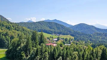 Malerischer Ausblick auf eine weite grüne Landschaft mit bewaldeten Bergen und Tälern unter blauem Himmel.