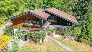 Traditionelles Holzhaus im Chalet-Stil, eingebettet in eine grüne, bewaldete Umgebung mit Satteldach.